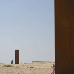 Unrecognizable female traveler standing near contemporary minimalist sculpture against cloudless blue sky in desert of Qatar